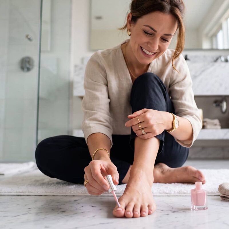 Frau lackiert sich zu Hause die Zehennägel – Nagellack und Nagelpilz als Thema der Nagelpflege